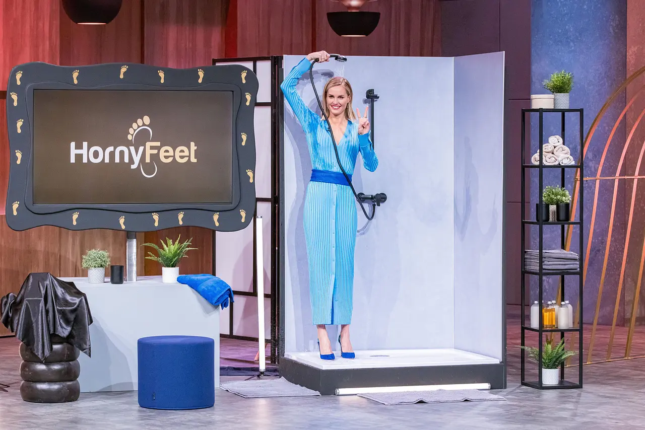 Warum eine Dusche aufgebaut wurde, erfuhren die Investoren erst später. Janna Ensthaler steht im blauen Kleid und in farblich passenden Highheels unter einer Dusche im Die Höhle der Löwen-Studio. - Foto: RTL / Bernd-Michael Maurer