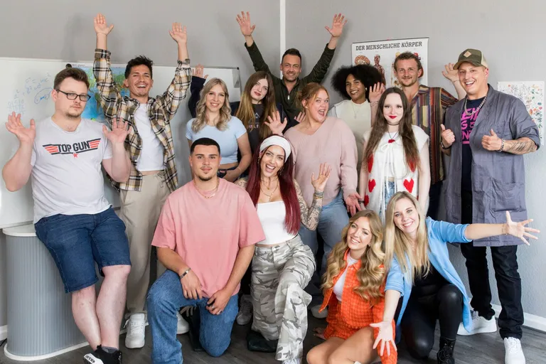 Der Cast vom Serien-Comeback "Krass Schule" lächelt in die Kamera, dabei strecken neue und altbekannte Gesichter die Hände nach oben. 