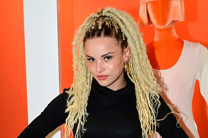 Christin Okpara mit blonden Braids und schwarzem Outfit vor einem rot-weißen Hintergrund, während eines öffentlichen Auftritts. In ihrer Instagram-Story verrät sie jetzt, wieso sie bei "Kampf der Realitystars" so plötzlich verschwunden ist.