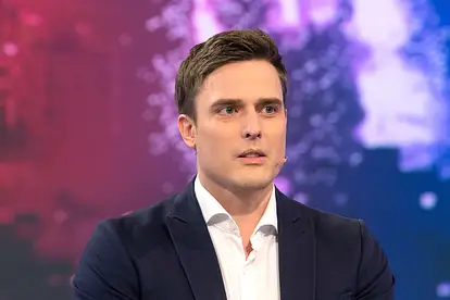 Constantin Schreiber blickt an der Kamera vorbei. Er trägt einen Anzug, hinter ihm ist eine bunte LED-Wand.