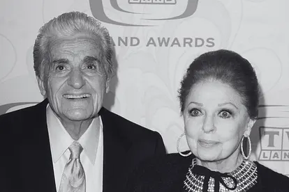 Tom Troupe und seine Ehefrau Carole Cook bei einem Event. Die beiden stehen Arm in Arm auf dem Red Carpet und lächeln.
