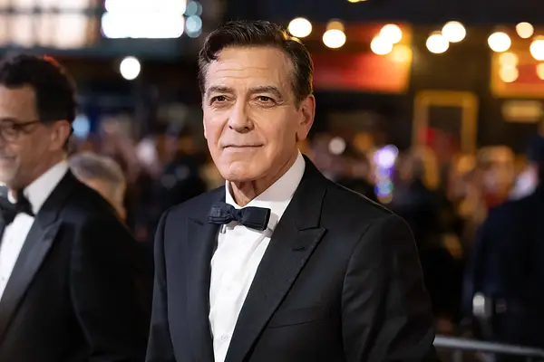 Man sieht George Clooney bei einer Veranstaltung. Er trägt schwarzes Haar mit einem grauen Verlauf, ein schwarzes Jackett und eine schwarze Fliege.
