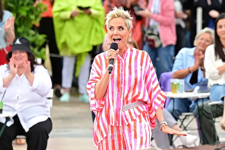 Inka Bause performt in einem gestreiften Outfit mit Mikro in der Hand auf der Bühne.