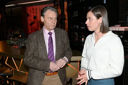 Jo Gerner und Matilda stehen vor einem Bartresen nebeneinander und sehen sich an.
