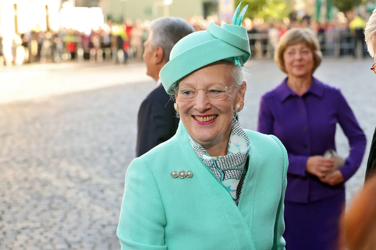 Königin Margrethe II. von Dänemark trägt ein mintgrünes Kostüm mit passendem Hund und lächelt an der Kamera vorbei.