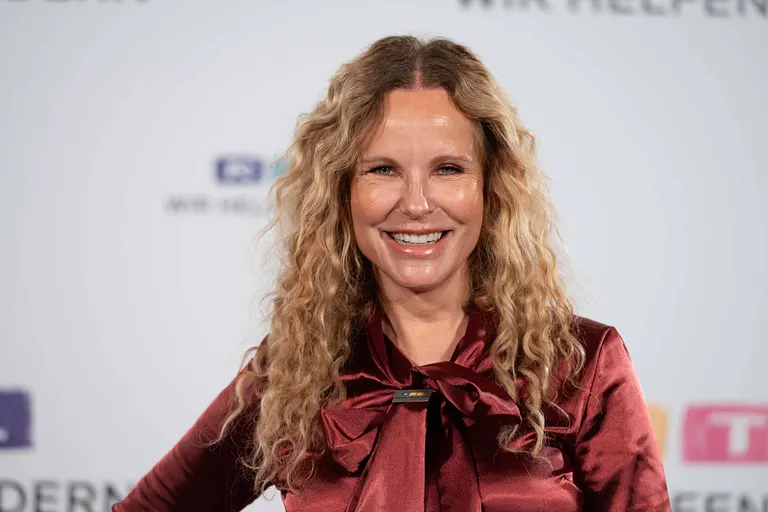 Katja Burkard auf dem roten Teppich beim RTL-Spendenmarathon "Wir helfen Kindern". Sie steht vor einer weißen Wand mit RTL-Logos und lächelt in die Kamera.