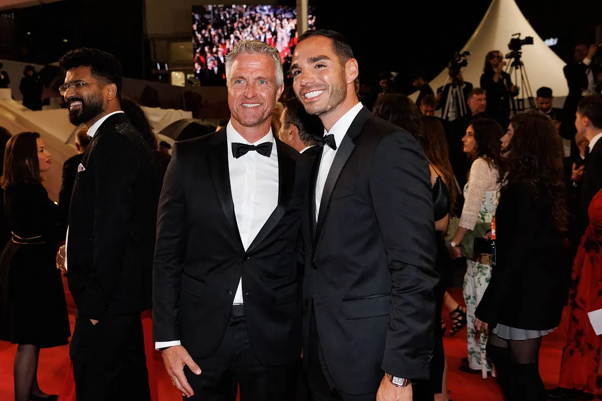 Ralf Schumacher und Lebensgefährte Étienne auf den Cannes Filmfestspielen. Beide lächeln in die Kamera und tragen einen schwarzen Anzug. 