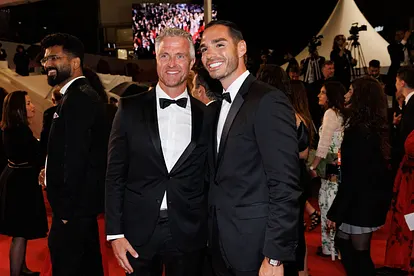 Ralf Schumacher und Lebensgefährte Étienne auf den Cannes Filmfestspielen. Beide lächeln in die Kamera und tragen einen schwarzen Anzug. 