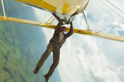 Tom Cruise hängt als Ethan Hunt an einem gelben Flugzeug, das kopfüber fliegt.