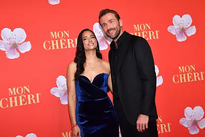 Amira Aly und Christian Düren posieren auf dem roten Teppich. Sie trägt ein dunkelblaues Samtkleid und er einen schwarzen Anzug.