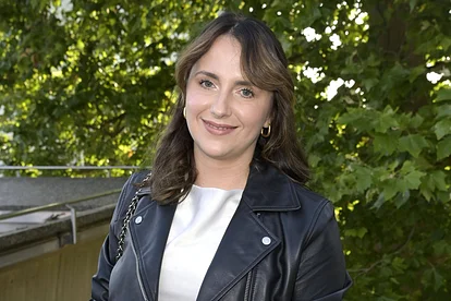 Anna Heiser posiert in Lederjacke vor einem Baum und lächelt