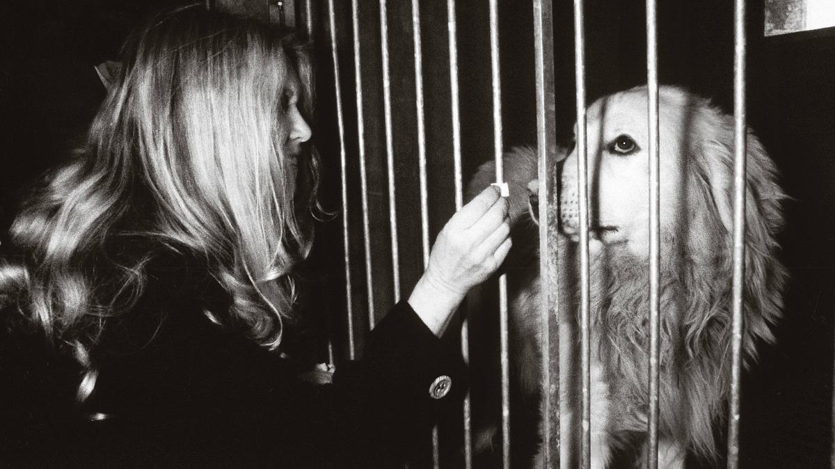 Brigitte Bardot vor einem Käfig, in dem ein Hund steckt.