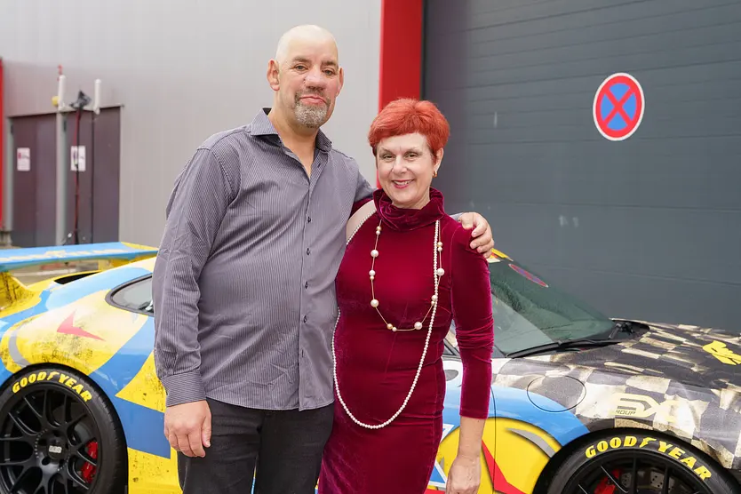Bauer Uwe und seine Frau Iris stehen Arm in Arm vor einem Auto und blicken in die Kamera.