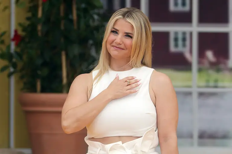 Beatrice Egli steht in einem weißen Outfit auf der Bühne und hat die Hand auf die Brust gelegt.