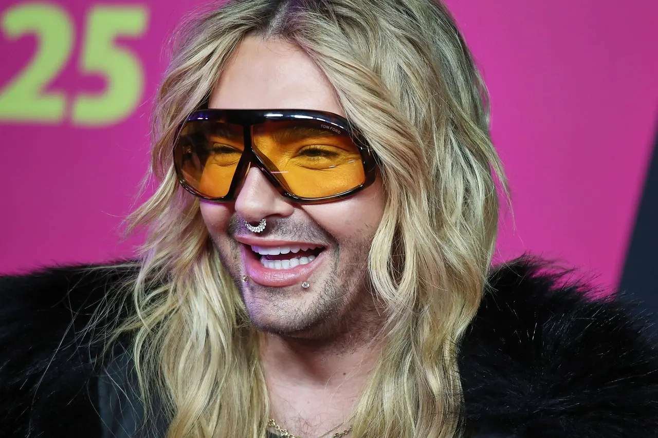 Bill Kaulitz trägt offene Haare und eine schwarze Sonnenbrille mit gelben Gläsern. Er lacht fröhlich. - Foto: IMAGO / dts Nachrichtenagentur Bill Kaulitz trägt offene Haare und eine schwarze Sonnenbrille mit gelben Gläsern. Er lacht fröhlich.