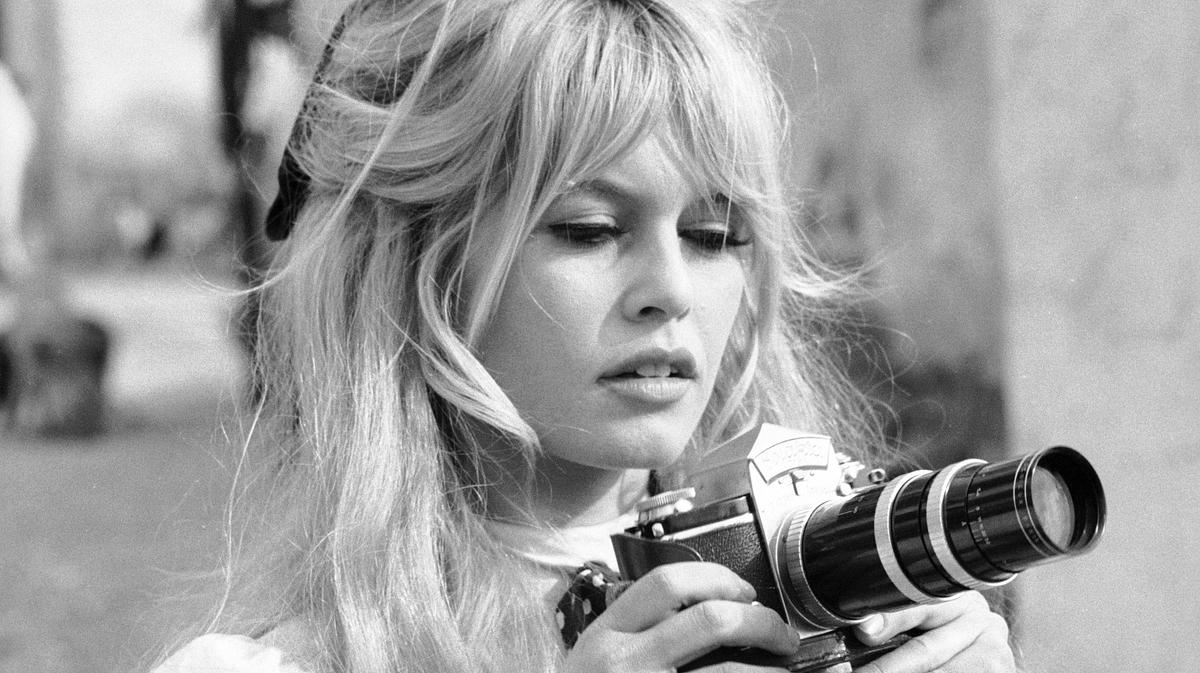 Brigitte Bardot hält eine Kamera in den Händen.