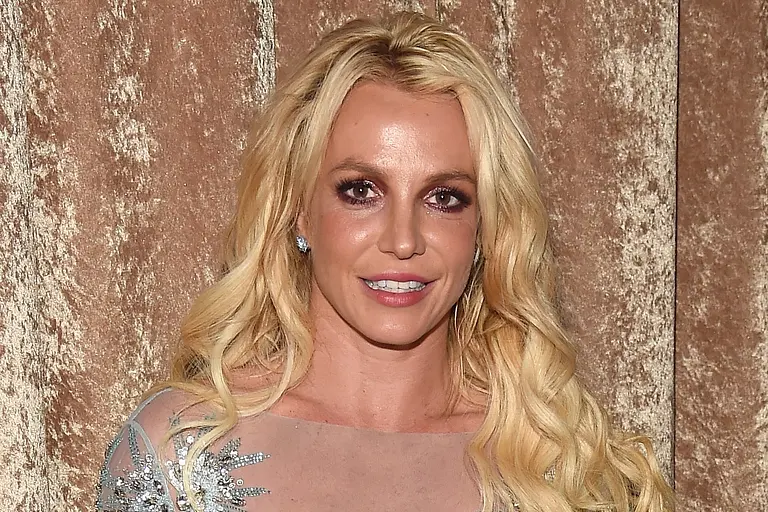 Britney Spears steht vor einem goldenen Samtvorhang und lächelt in die Kamera.