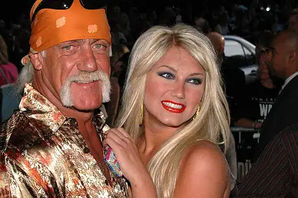 Hulk Hogan lächelt bei einem Event in die Kamera, seine Tochter Brooke drückt sich an ihn.