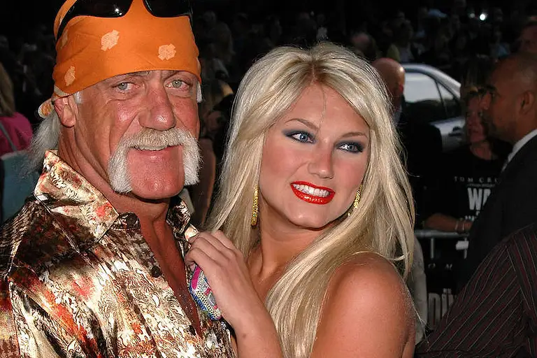 Hulk Hogan lächelt bei einem Event in die Kamera, seine Tochter Brooke drückt sich an ihn.
