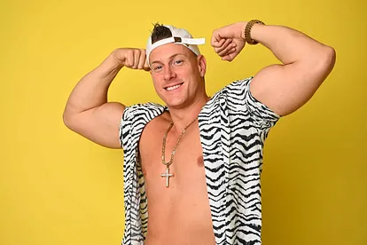 Calvin Kleinen posiert lächelnd und oberkörperfrei im Zebra-Hemd und präsentiert seinen Bizeps