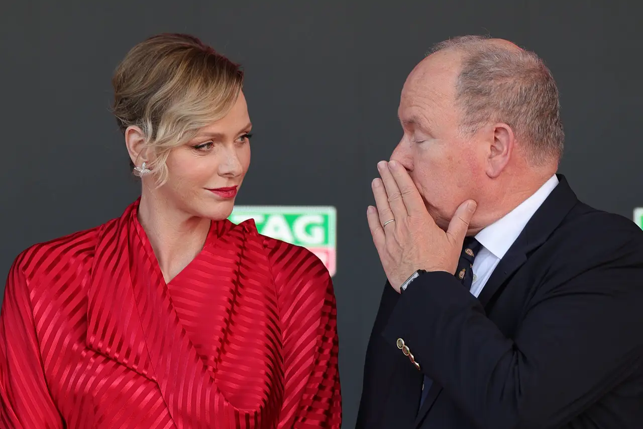 Charlène von Monaco trägt beim Grand Prix ein rotes Kleid. Fürst Albert scheint ihr etwas zuzuflüstern.