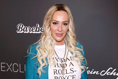 Cora Schumacher trägt offene, gelockte Haare, ein weißes T-Shirt und einen türkisen Blazer. Sie lächelt sanft.