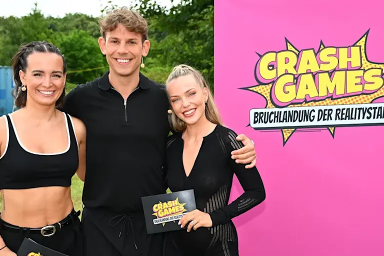 Die neuen Feldreporter Julia Römmelt, Max Weißenböck und Laura Maria Rypa schauen lächelnd in die Kamera. Mit Moderationskarten und neben dem großen Logo von "Crash Games" sind sie bereit für die neue Staffel!