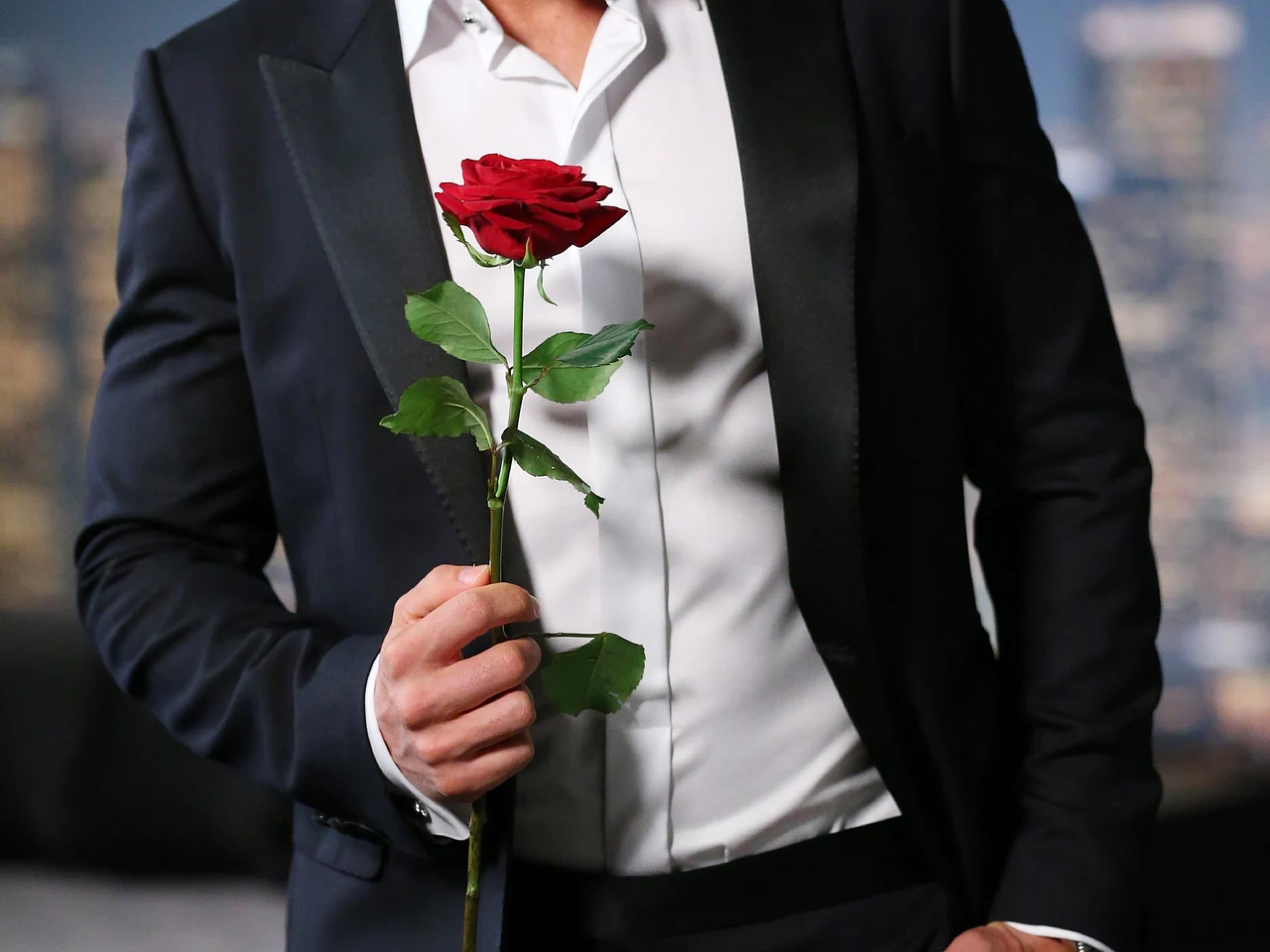 Mann im Anzug hält eine rote Rose in der Hand.
