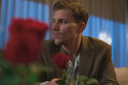 Bachelor Felix Stein schaut nachdenklich in eine Richtung, vor ihm sind verschwommen zwei Rosen