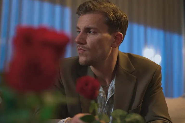 Bachelor Felix Stein schaut nachdenklich in eine Richtung, vor ihm sind verschwommen zwei Rosen
