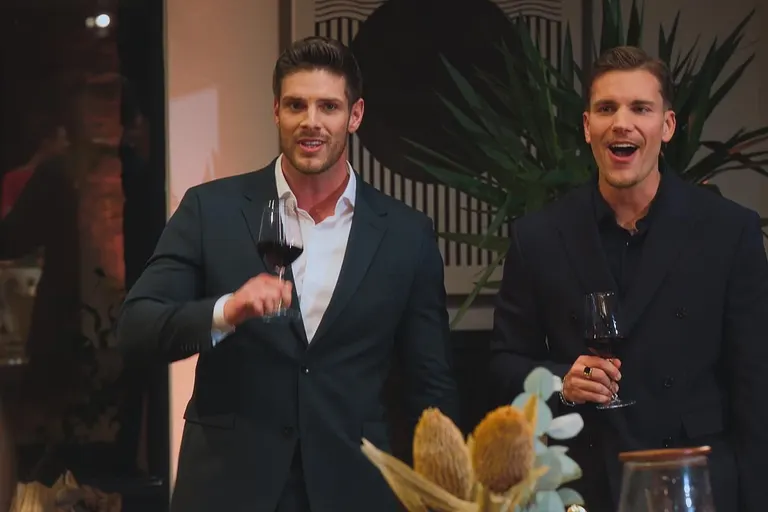 Martin (links) und Felix (rechts) mit überraschendem Gesichtsausdruck in einem blauen und schwarzen Anzug und mit einem Glas in der Hand.