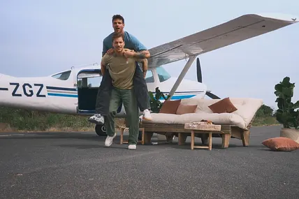 Felix nimmt Martin vor einem Flugzeug Huckepack. 