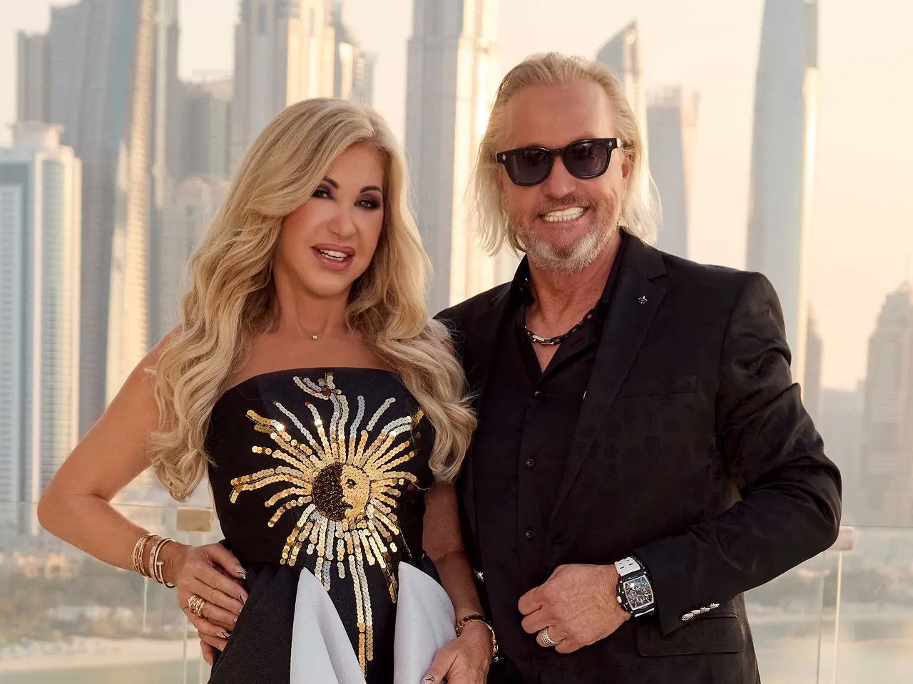 Robert und Carmen Geiss stehen elegant gekleidet nebeneinander und lächeln breit in die Kamera.