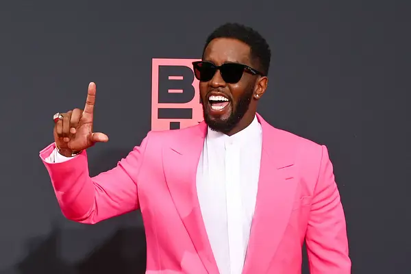 Sean Combs auf dem roten Teppich. Er lacht und trägt eine Sonnenbrille, mit Daumen und Zeigefinger der rechten Hand formt er ein 'L'.
