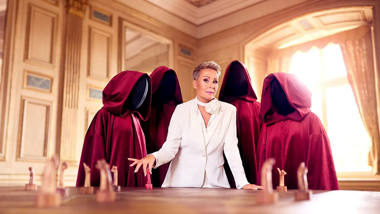 Die Verräter - Sonja Zietlow Sonja Zietlow ist umgeben von gesichtslosen Personen in roten Roben. Vor ihr steht ein Schachbrett. - Foto: RTL / Benno Kraehahn