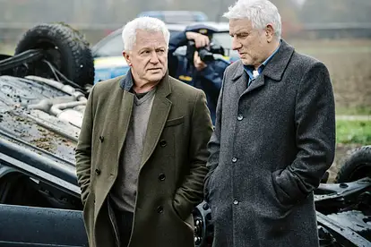 Miroslav Nemec und Udo Wachtveitl stehen vor einem Autowrack.