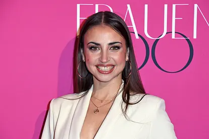 Ekaterina Leonova trägt einen weißen Blazer und stahlt vor einem pinken Hintergrund in die Kamera. Sie schwebt auf Wolke 7!