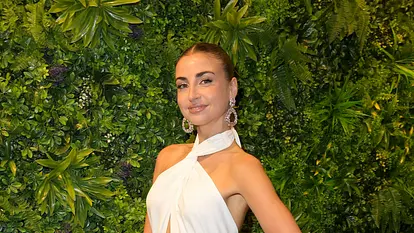 Ekaterina Leonova posiert in weißem Kleid vor einer begrünten Wand