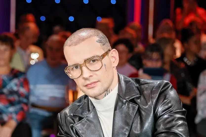 Eric Stehfest, hier mit schwarzer Lederjacke und brauner Brille zu sehen, blickt ernst in die Kamera.