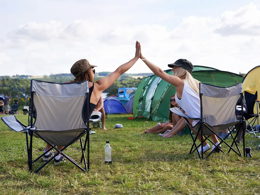 Zwei Frauen auf einem Campingplatz in Anglerstühlen geben sich ein High Five Zwei Frauen auf einem Campingplatz in Anglerstühlen geben sich ein High Five