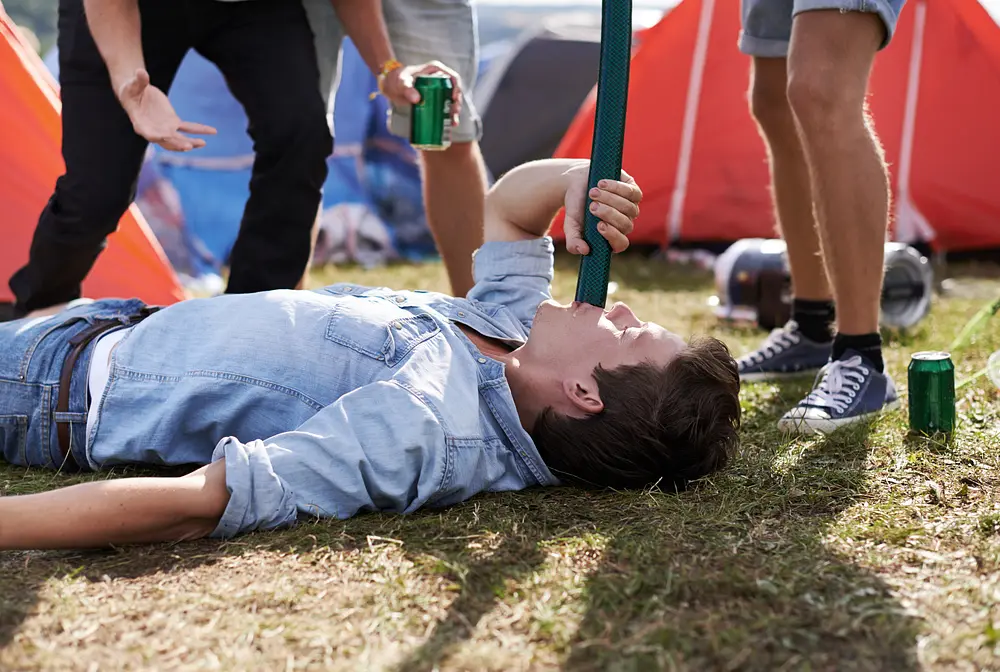 Aufnahme eines Mannes, der Bier durch eine Röhre trinkt, während seine Freunde daneben stehen