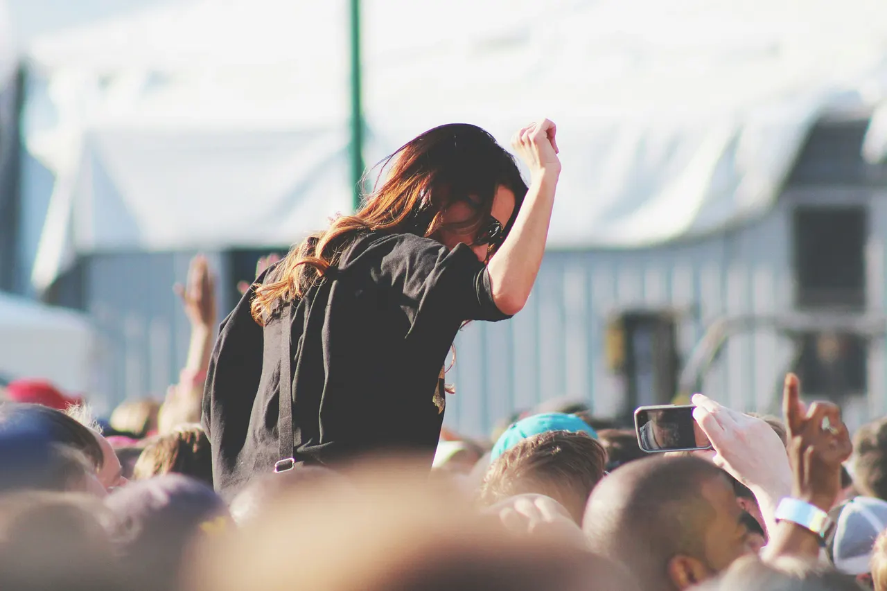festivalkalender-2025 Frau auf einem Festival mit einem Arm in der Luft - Foto: Unsplash/Joey Thompson