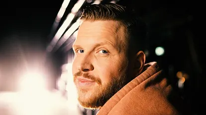 Rapper FiNCH schaut über die Schulter lächelnd in die Kamera.