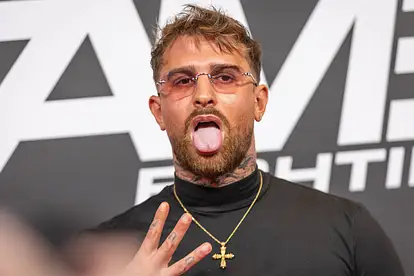 Gigi Birofio im schwarzen Turtleneck mit Sonnenbrille und Kreuzkette. Er zeigt drei Finger in die Kamera und dreckt die Zunge raus. 