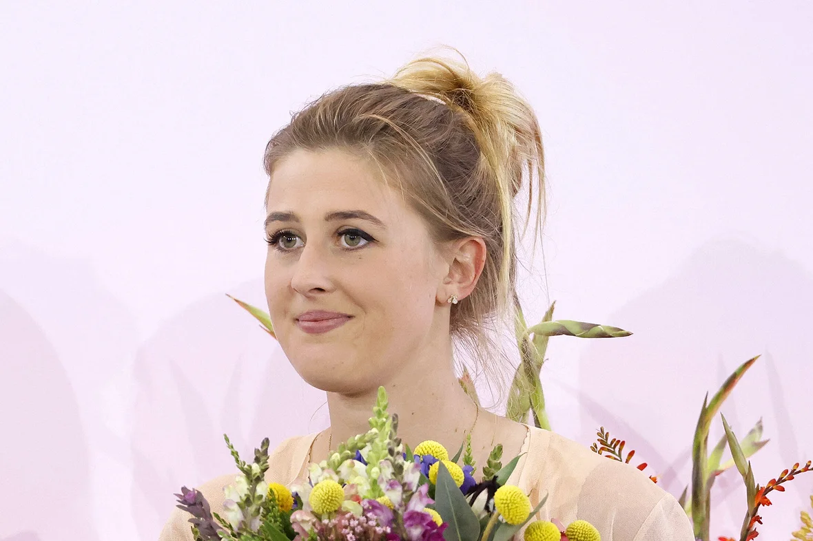Gina Schumacher lächelt, mit einem Blumenstrauß in der Hand.