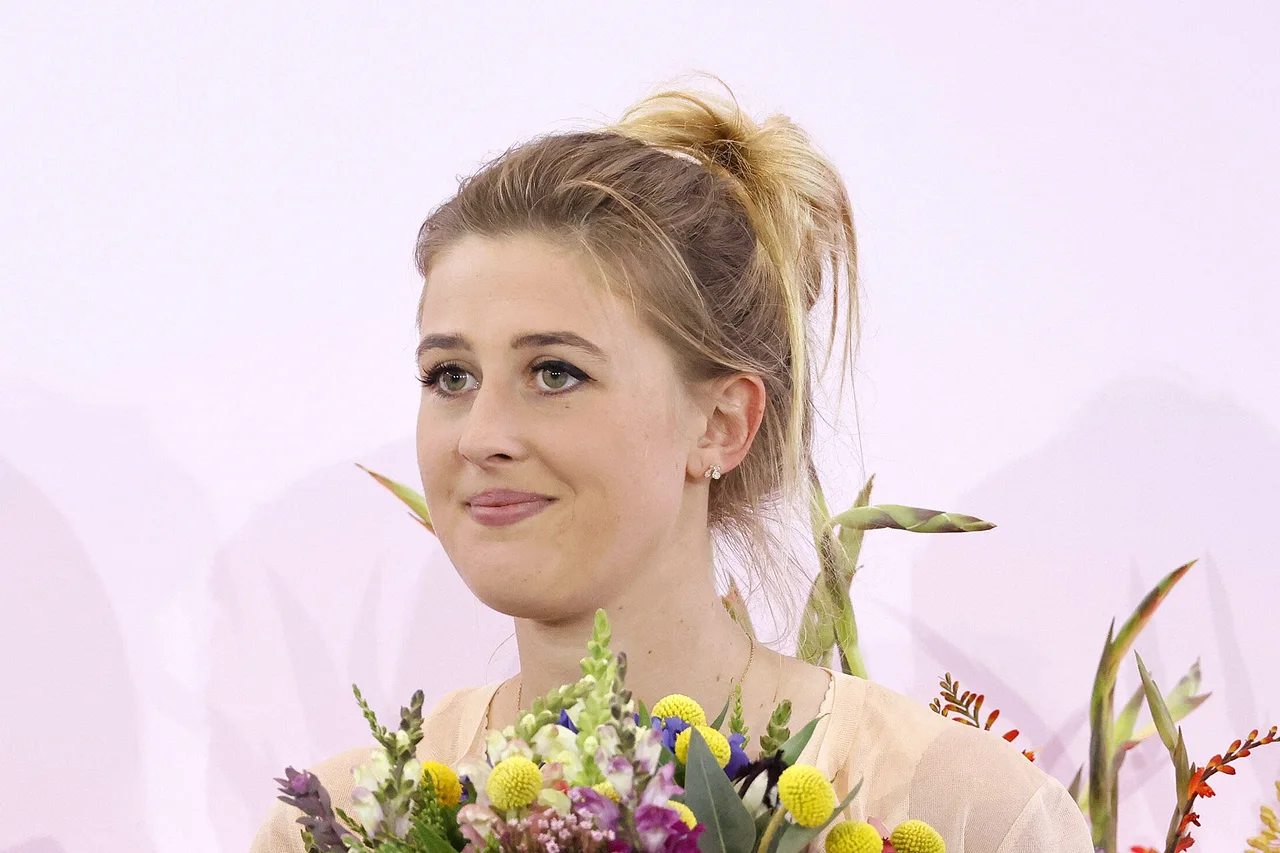 Gina Schumacher lächelt, mit einem Blumenstrauß in der Hand.
