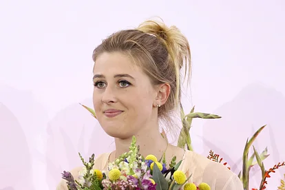 Gina Schumacher lächelt, mit einem Blumenstrauß in der Hand.