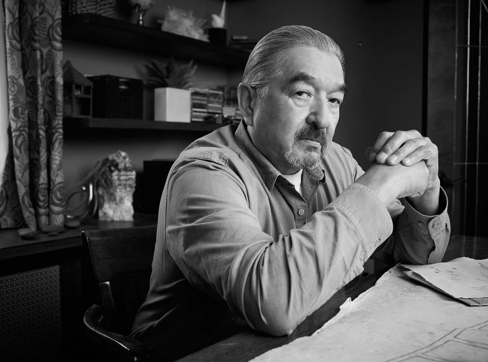 Graham Greene sitzt an einem Tisch und schaut ernst in die Kamera Graham Greene sitzt an einem Tisch und schaut ernst in die Kamera