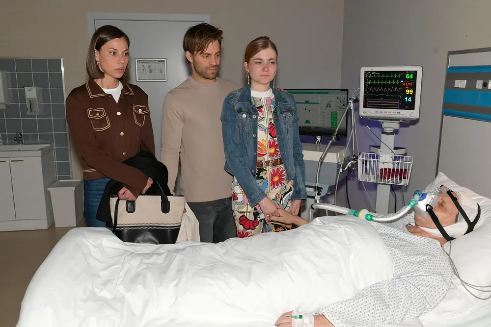 Matilda, Julian und Johanna stehen am Krankenbett von Gerner, der beatmet wird. Matilda, Julian und Johanna stehen am Krankenbett von Gerner, der beatmet wird.