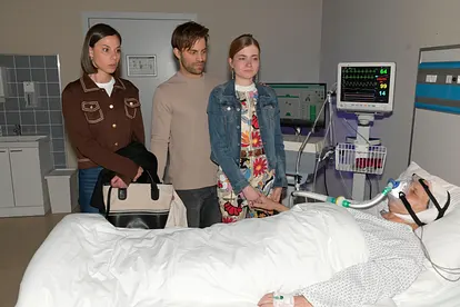 GZSZ-Szene: Matilda, Julian und Johanna stehen besorgt an Gerners Krankenbett. Er liegt am Beatmungsgerät und liegt im Koma.